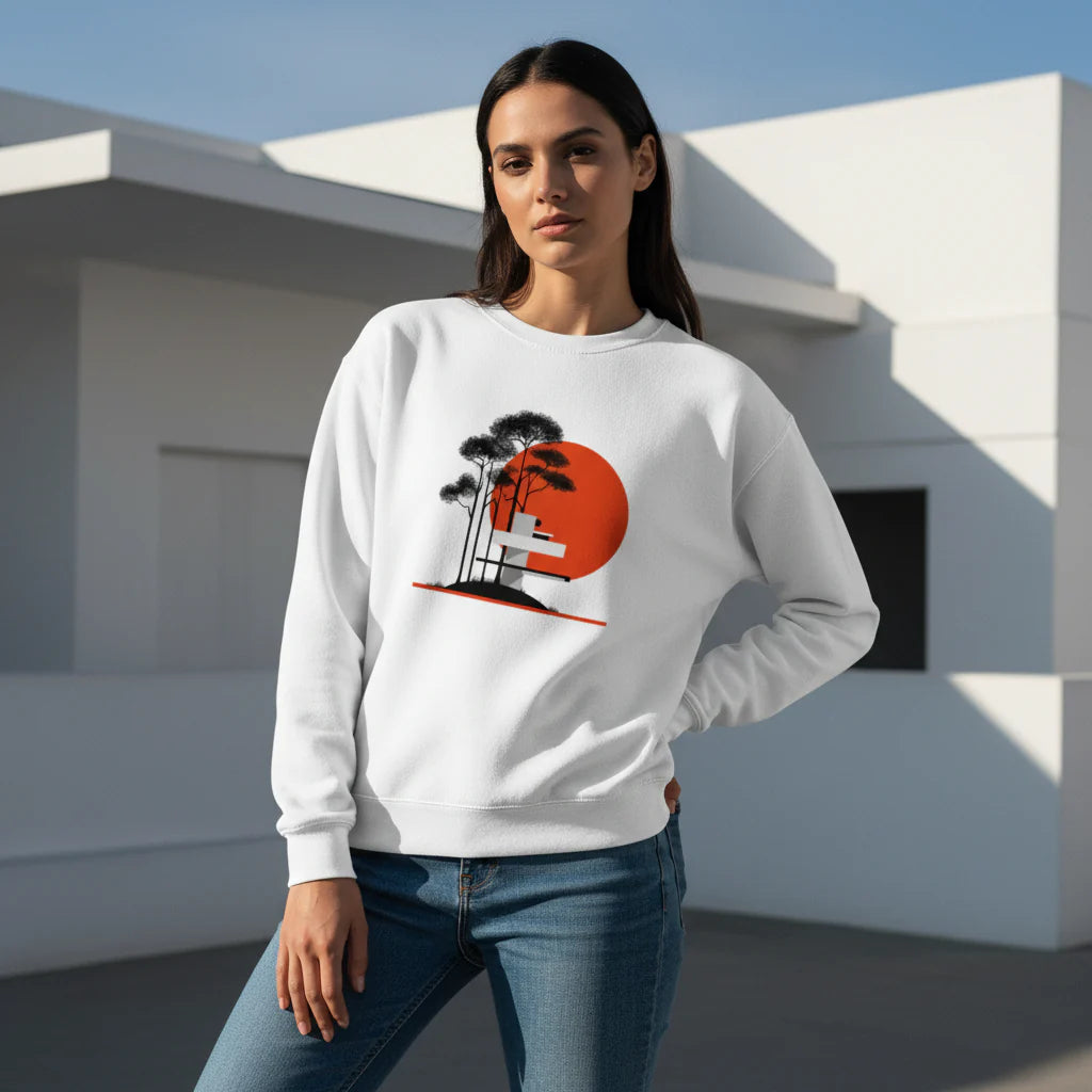 Woman wearing a white sweatshirt with a graphic design of palm trees and a sunset, standing in front of a modern building.